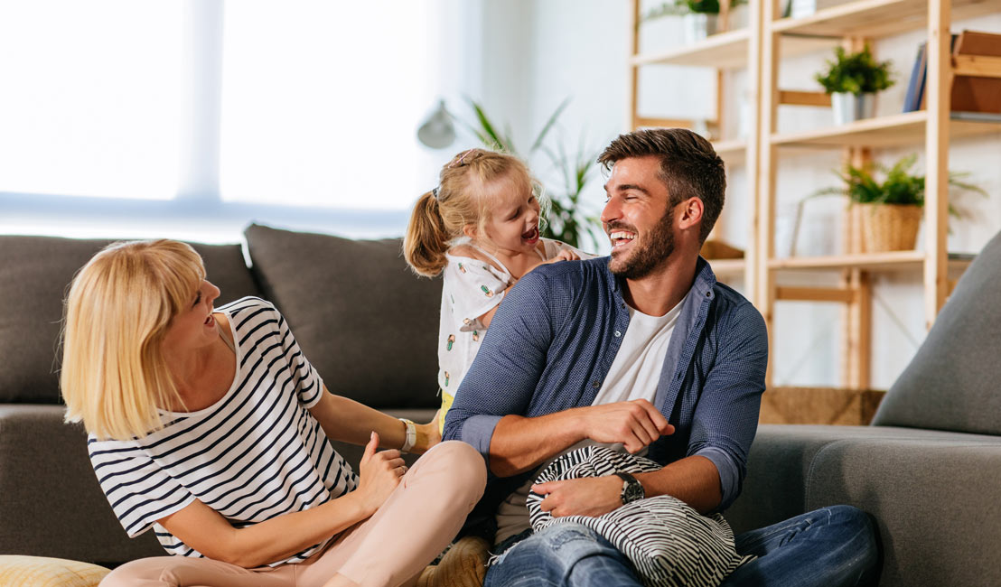 Parents sitting on the floor with their daughter popping up behind them Parents sitting on the floor with their daughter popping up behind them